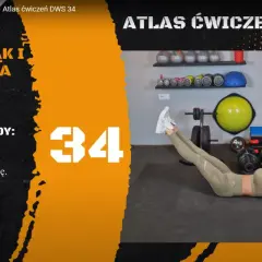 Kobieta wykonuje ćwiczenie unoszenia rąk i nóg leżąc na plecach. W tle siłownia z akcesoriami do treningu.