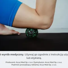 Masażysta ugniata czworogłowy uda za pomocą zielonej piłeczki do masażu na czarnej macie.