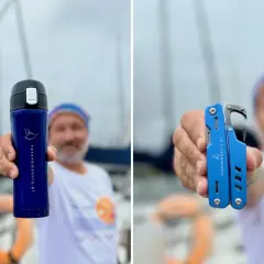 Mężczyzna na tle żaglówek podczas regat trzyma niebieski kubek termiczny i multitool.
