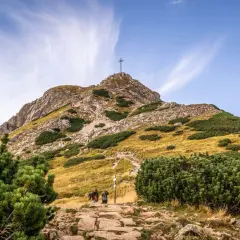 Kamienista ścieżka prowadzi pod górę, gdzie widać krzyż na szczycie. Turyści idą w stronę, by zobaczyć, ile ma Giewont.