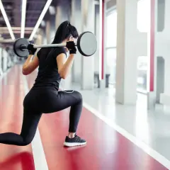 Kobieta wykonuje wykroki ze sztangą. Efektywny trening siłowy dla kobiet.