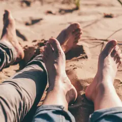 Dwie pary **bare foot** leżą na piaszczystej plaży, ciesząc się słońcem i ciepłem piasku.