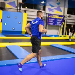 Mężczyzna w niebieskiej koszulce i czarnych spodenkach biegnie po trampolinach, wykonując trening interwałowy.