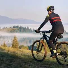 Rowerzysta w kasku i sportowym stroju pokonuje górski szlak. Jego rytmiczna kadencja i błotniste opony świadczą o trudnej trasie.