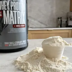 Puszka odżywki białkowej "Whey Protein Matrix" i miarka z proszkiem, gotowe do przygotowania białko po treningu.