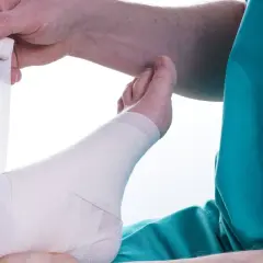 Opatrywanie stopy po kontuzji. Ręce owijają bandażem kostkę i stopę.