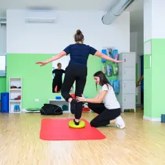 Fizjoterapeutka pomaga pacjentce ćwiczyć równowagę na dysku balansującym, doskonaląc propriocepcję.