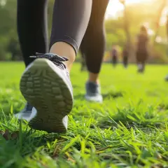 Grupa osób uprawia power walking po zielonej trawie w parku, w promieniach zachodzącego słońca.