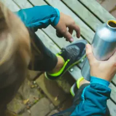Osoba w sportowym ubraniu trzyma metalową butelkę z izotonikiem, gotowa do uzupełnienia płynów po treningu.