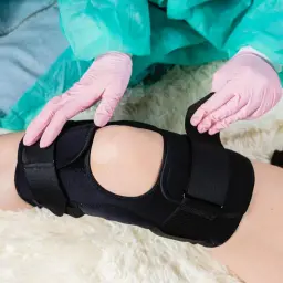 Ręce w różowych rękawiczkach dopasowują stabilizator na kolanie.