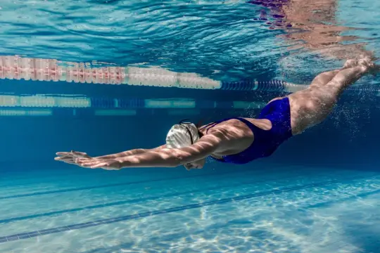 Kobieta w niebieskim stroju pływackim nurkuje pod wodą w basenie, doskonale prezentując sporty wodne.