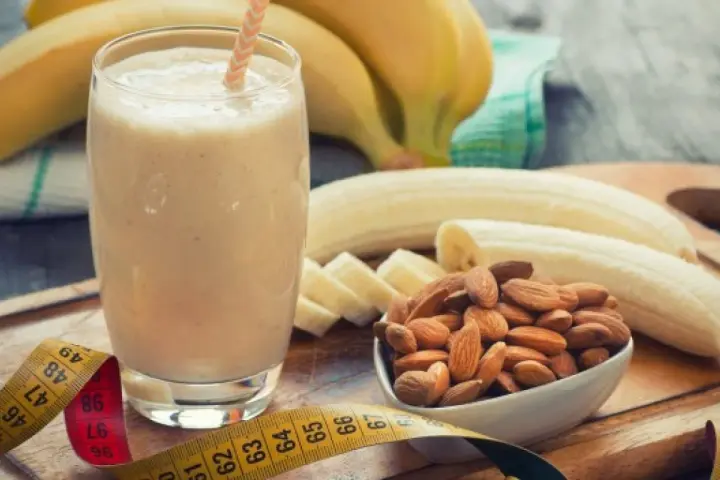 Pyszny szejk proteinowy z bananem i migdałami, idealny na zdrowy początek dnia lub po treningu. Miarka krawiecka sugeruje, że to napój wspierający sylwetkę.