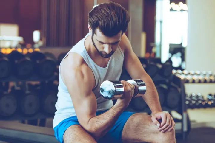 Mężczyzna ćwiczy biceps z hantlem w siłowni.