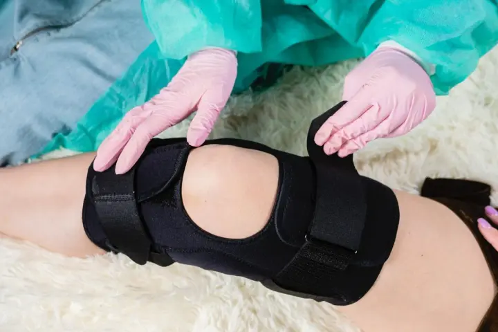 Ręce w różowych rękawiczkach dopasowują stabilizator na kolanie.