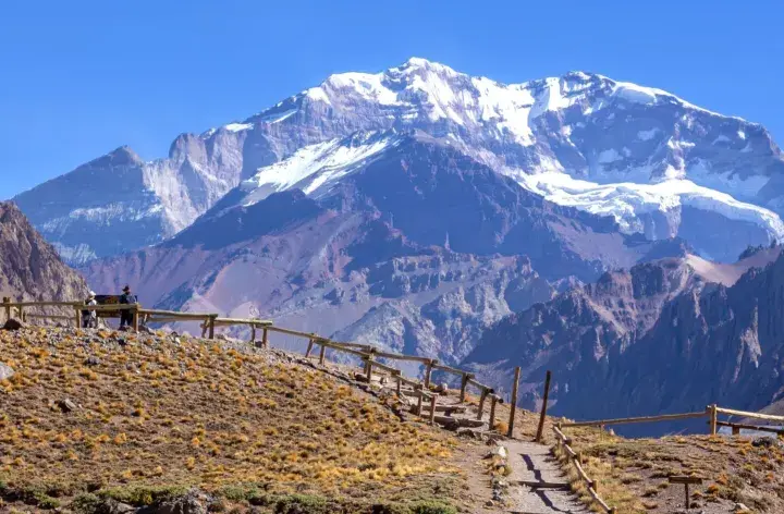 Aconcagua, najwyższy szczyt w Ameryce Południowej, góruje nad surowym krajobrazem. Ścieżka z drewnianym ogrodzeniem prowadzi przez suchą trawę.