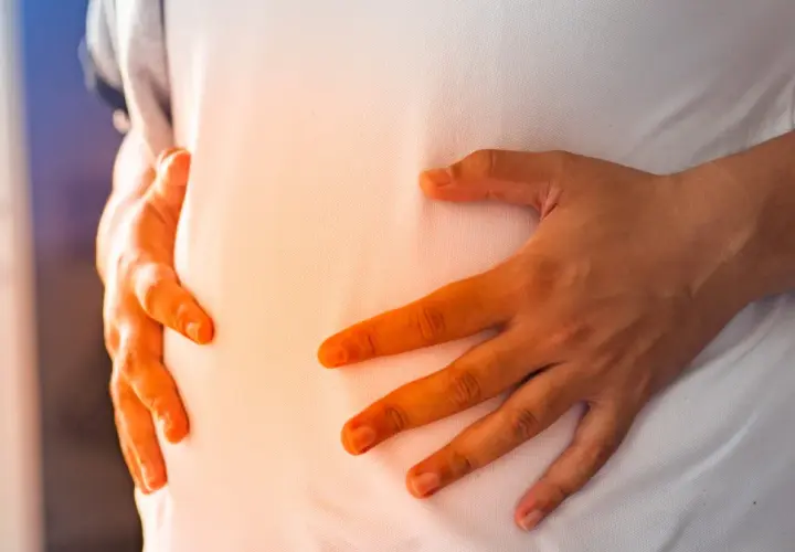 Dłonie obejmujące brzuch, sugerujące dyskomfort. Szukasz pomysłów, co jeść na bolący żołądek?