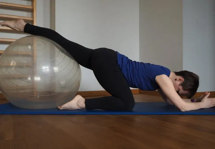 Kobieta na macie ćwiczy z piłką, rozciągając nogę. Widać, co daje stretching: lepsza gibkość i relaks.