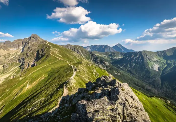 Malownicza ścieżka prowadzi na wejście na Kasprowy. Zielone zbocza Tatr pod błękitnym niebem z chmurami.
