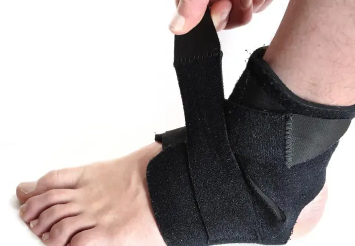 Dłoń zapina czarny stabilizator na kostce. Zapewnia wsparcie i ochronę podczas aktywności.