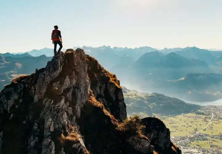 Alpinista na szczycie skalistej góry, podziwiający panoramę. Czy wejście na rysy jest trudne? Widok zapiera dech w piersiach, ale droga na górę wymaga wysiłku.