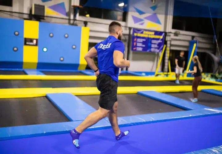 Mężczyzna w niebieskiej koszulce i czarnych spodenkach biegnie po trampolinach, wykonując trening interwałowy.