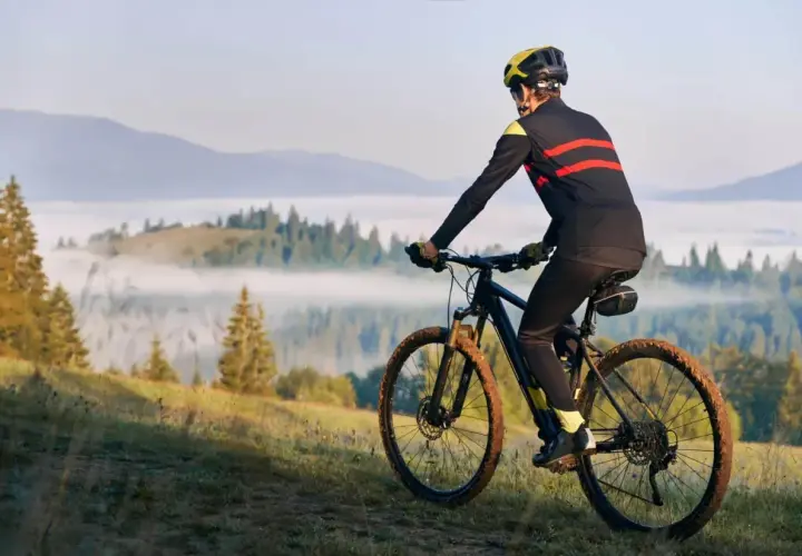 Rowerzysta w kasku i sportowym stroju pokonuje górski szlak. Jego rytmiczna kadencja i błotniste opony świadczą o trudnej trasie.