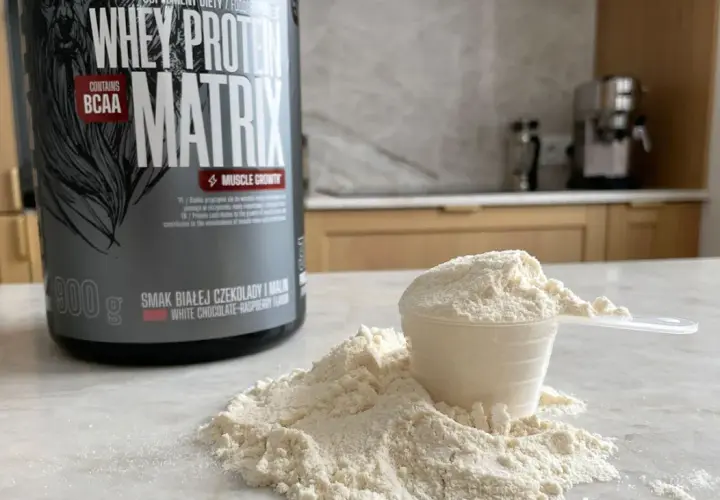 Puszka odżywki białkowej "Whey Protein Matrix" i miarka z proszkiem, gotowe do przygotowania białko po treningu.