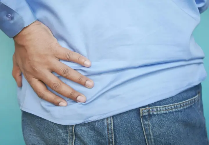 Dłoń uciska ból w okolicy bioder, sugerując punkty spustowe mięśnia biodrowo-lędźwiowego.
