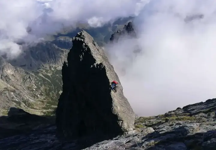 Wspinacz zdobywa skalisty szczyt, otoczony mgłami i majestatycznymi górami.