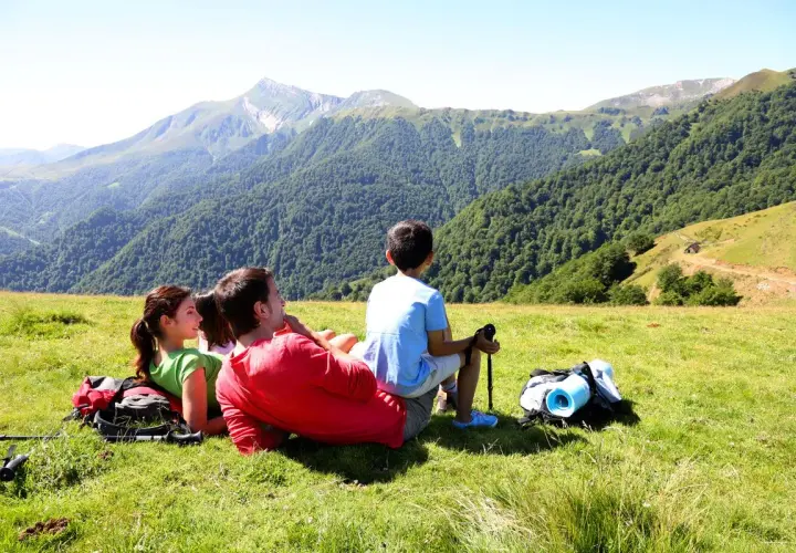 Rodzina odpoczywa na zielonej łące, podziwiając majowe Tatry. W tle gęsty las i skaliste szczyty.