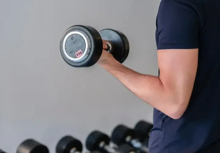 Mężczyzna ćwiczy biceps z hantlem 8 kg, realizując swój plan treningowy siłownia 3-dniowy.