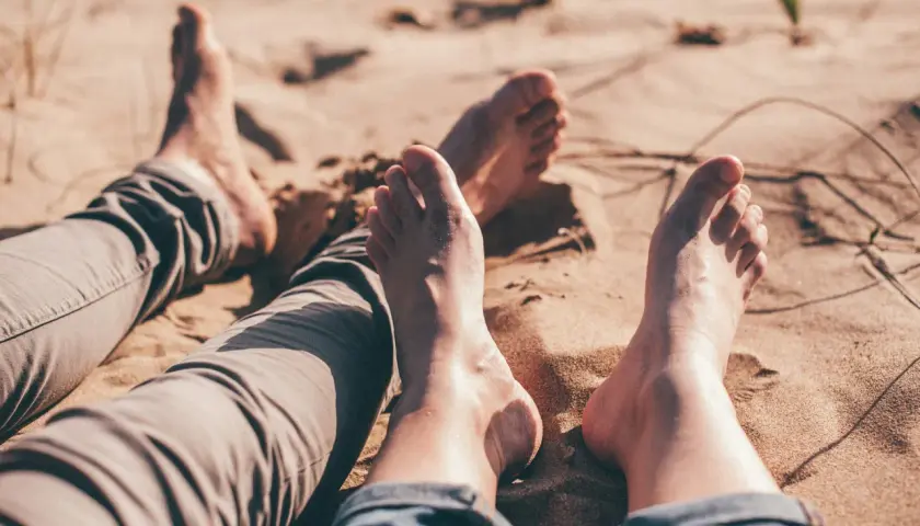 Dwie pary **bare foot** leżą na piaszczystej plaży, ciesząc się słońcem i ciepłem piasku.