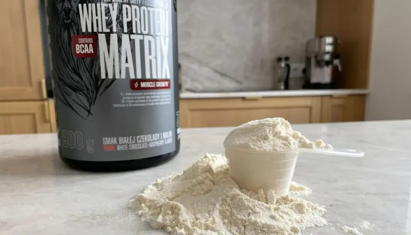 Puszka odżywki białkowej "Whey Protein Matrix" i miarka z proszkiem, gotowe do przygotowania białko po treningu.