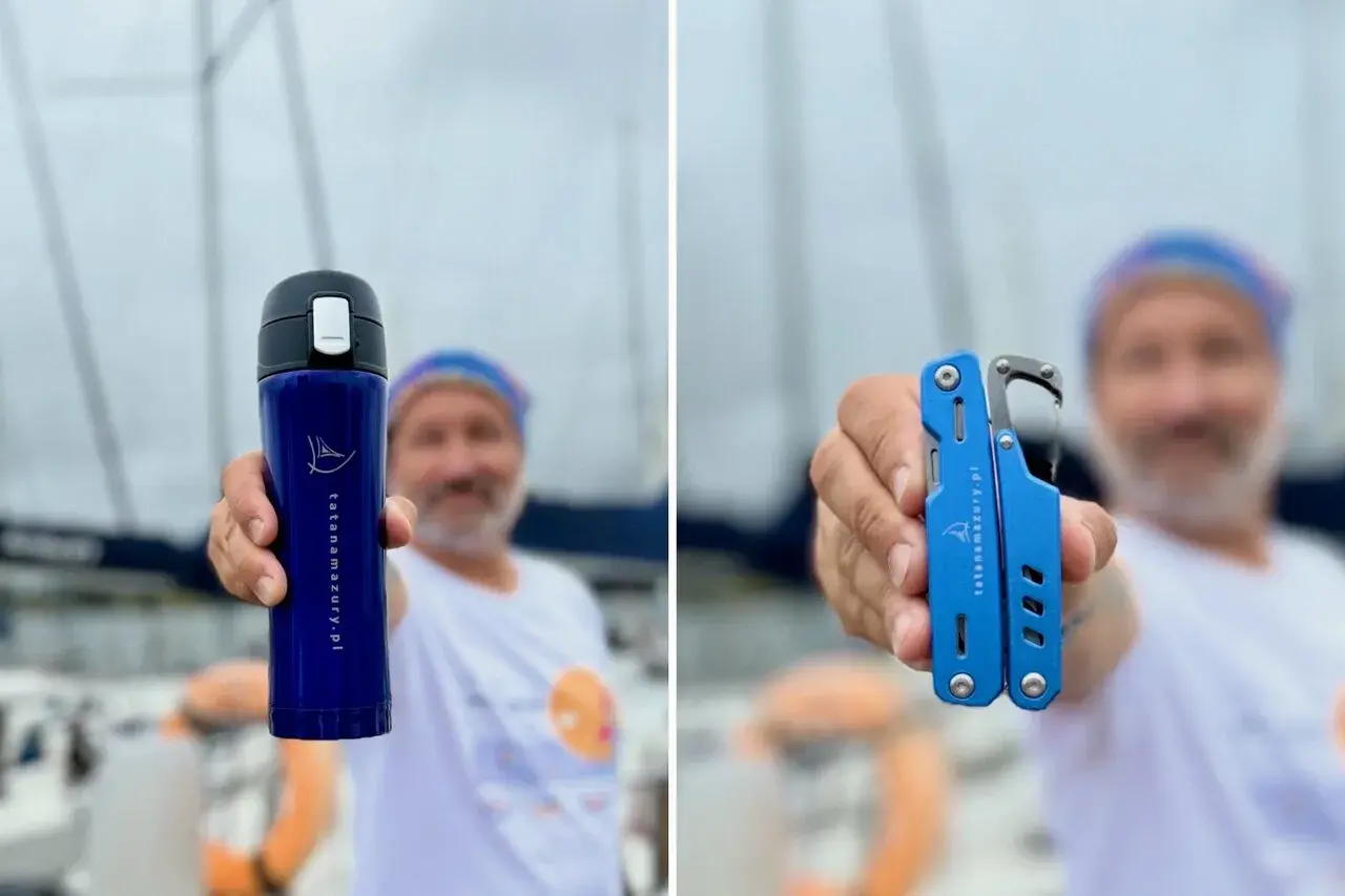 Mężczyzna na tle żaglówek podczas regat trzyma niebieski kubek termiczny i multitool.