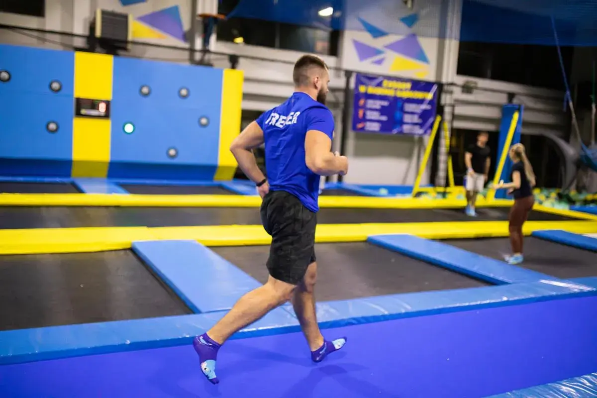 Mężczyzna w niebieskiej koszulce i czarnych spodenkach biegnie po trampolinach, wykonując trening interwałowy.