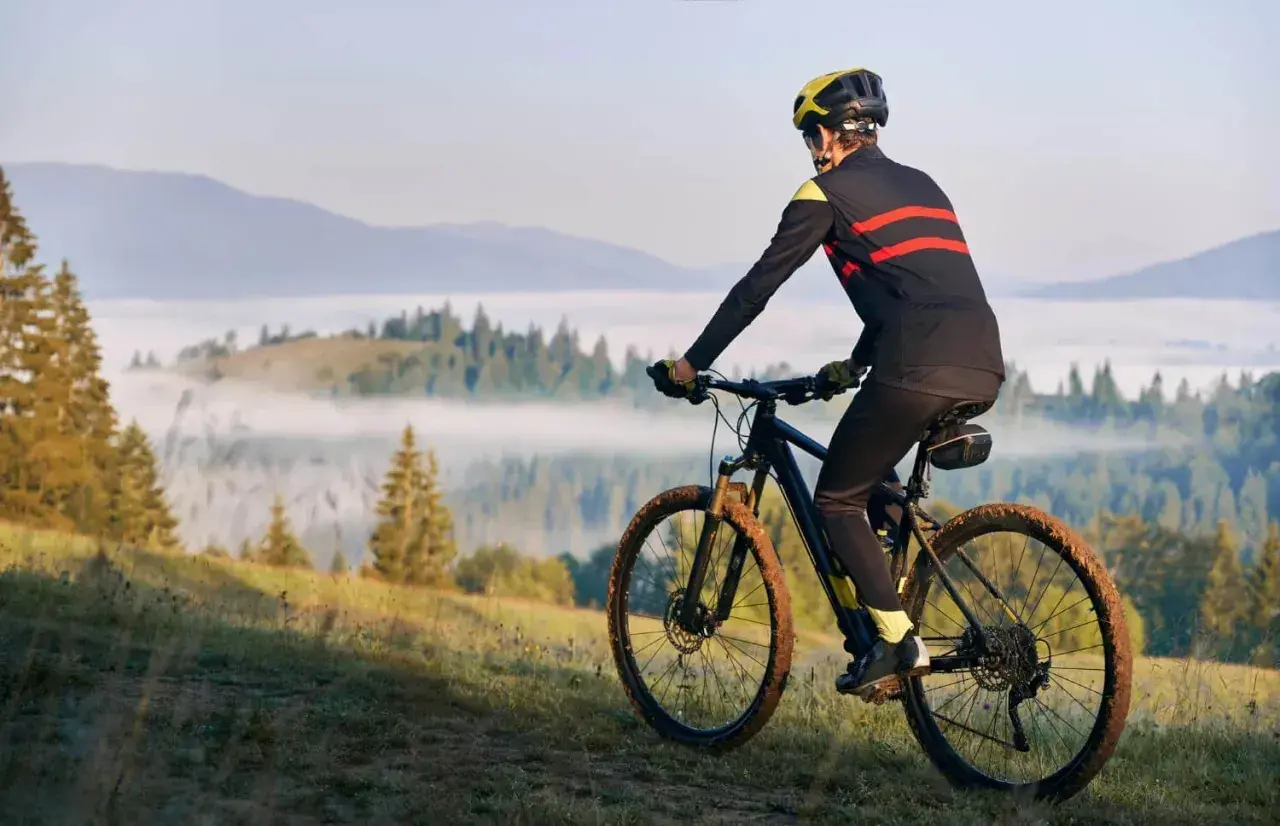 Rowerzysta w kasku i sportowym stroju pokonuje górski szlak. Jego rytmiczna kadencja i błotniste opony świadczą o trudnej trasie.