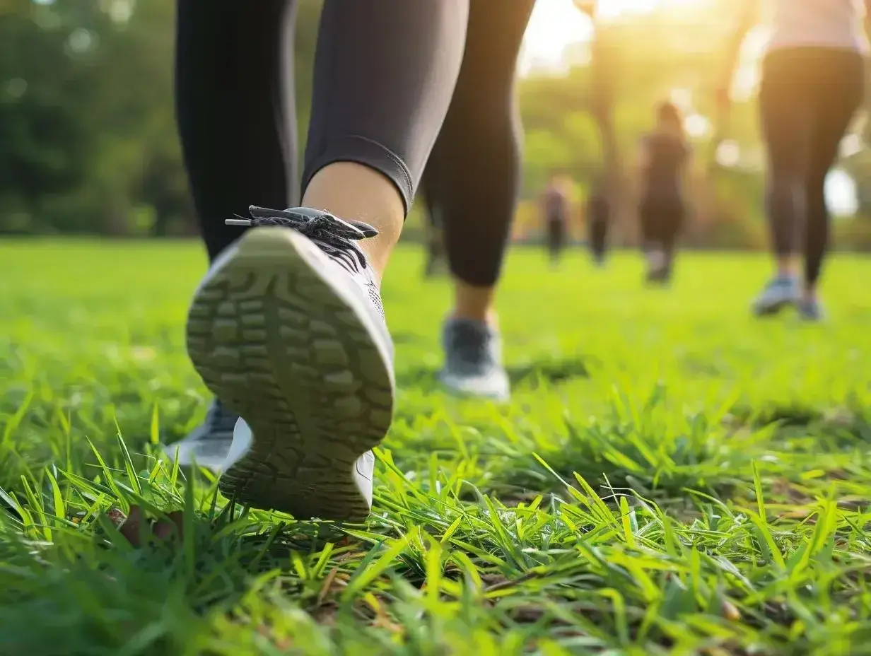 Grupa osób uprawia power walking po zielonej trawie w parku, w promieniach zachodzącego słońca.