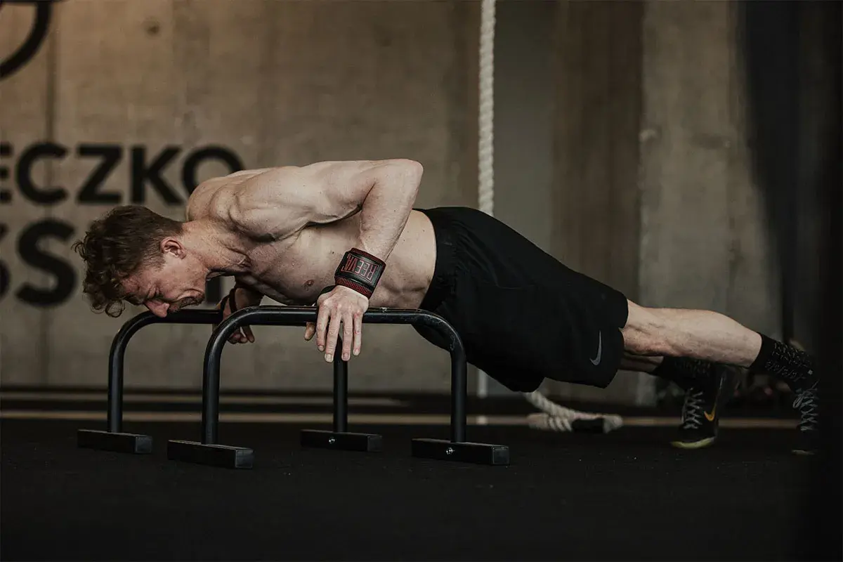 Mężczyzna wykonuje pompki na poręczach, ćwicząc siłę górnej części ciała. To część treningu push pull legs.