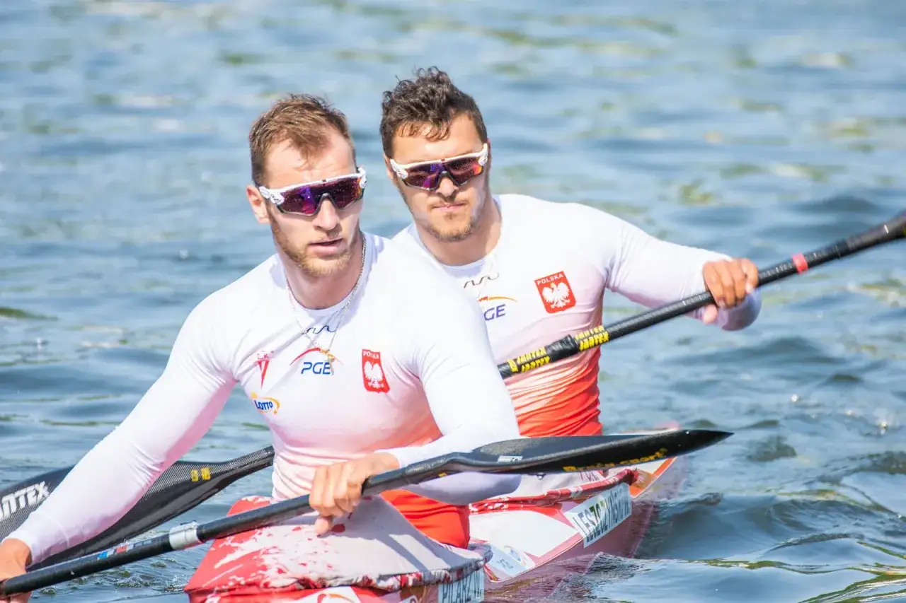 Dwóch polskich kajakarzy w biało-czerwonych strojach, gotowych do walki o tytuł mistrza Polski.
