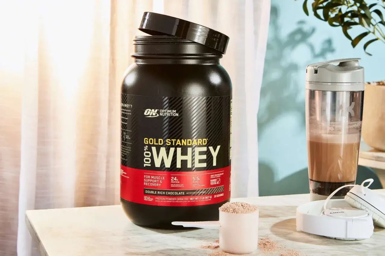 Białko serwatkowe co to? Duże opakowanie odżywki białkowej Optimum Nutrition Gold Standard 100% Whey, shaker z napojem i miarka z proszkiem.