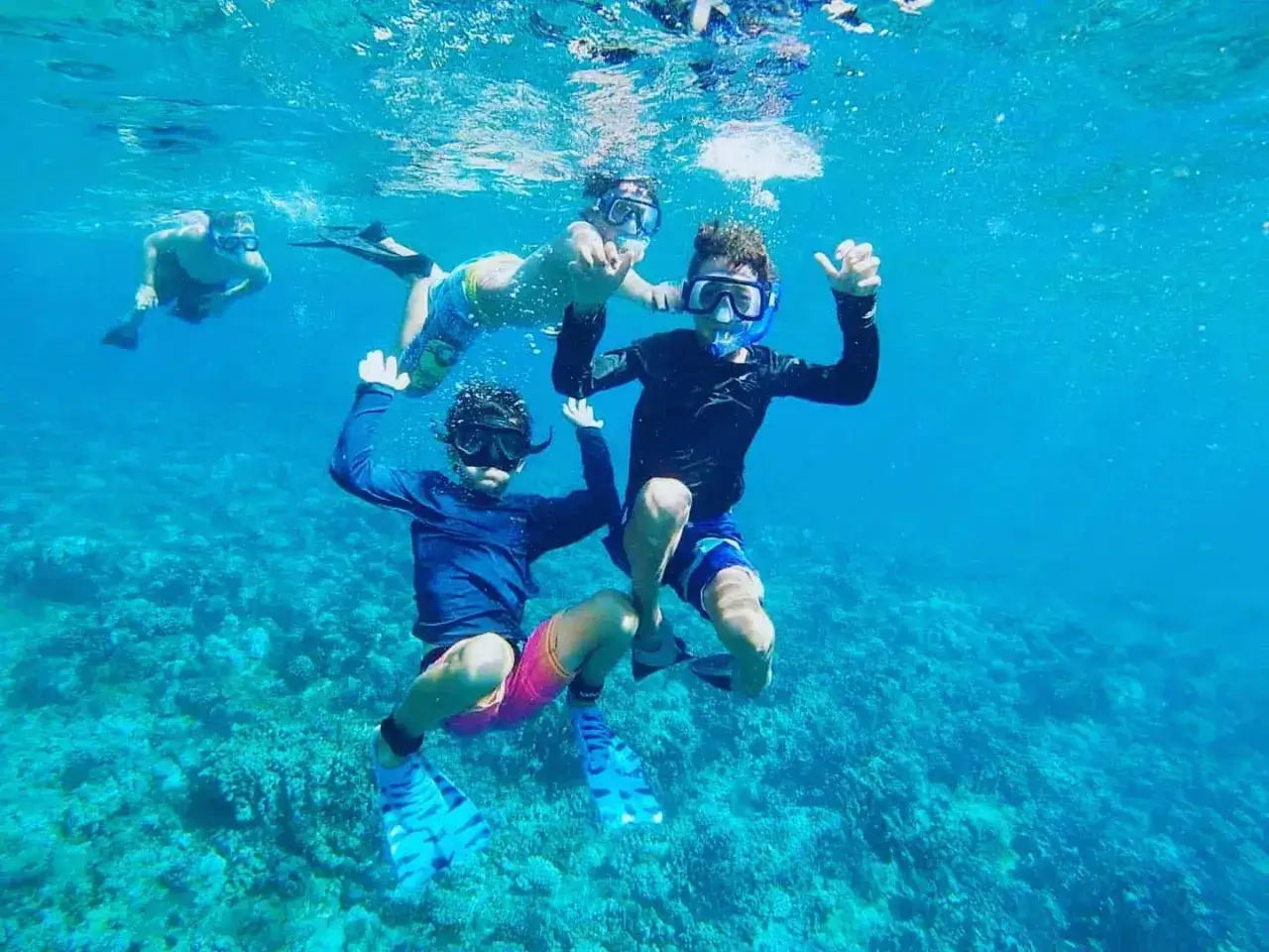 Dzieci cieszą się snorkelingiem, pływając w turkusowej wodzie nad rafą koralową.